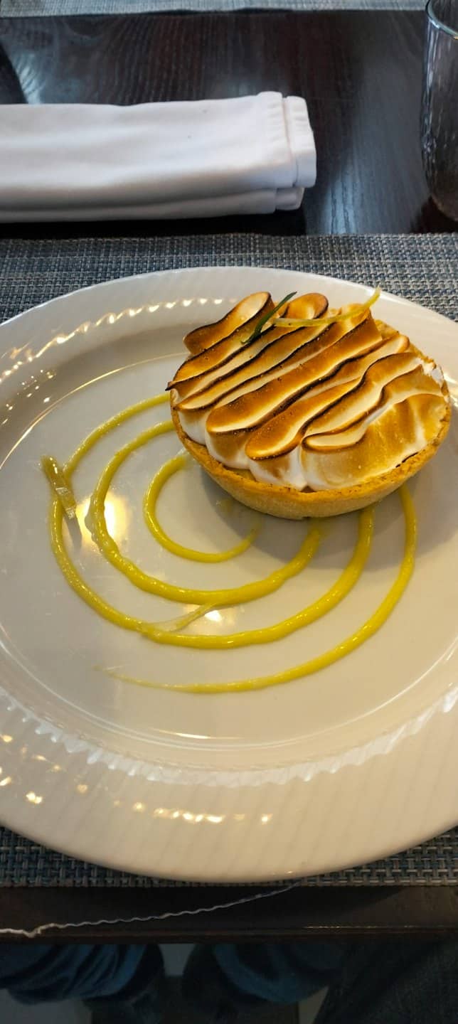 Tarta de limón y merengue servida en plato blanco con salsa.