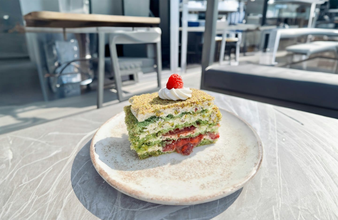 Una rebanada de pastel de pistacho y frambuesa en capas sobre un plato.